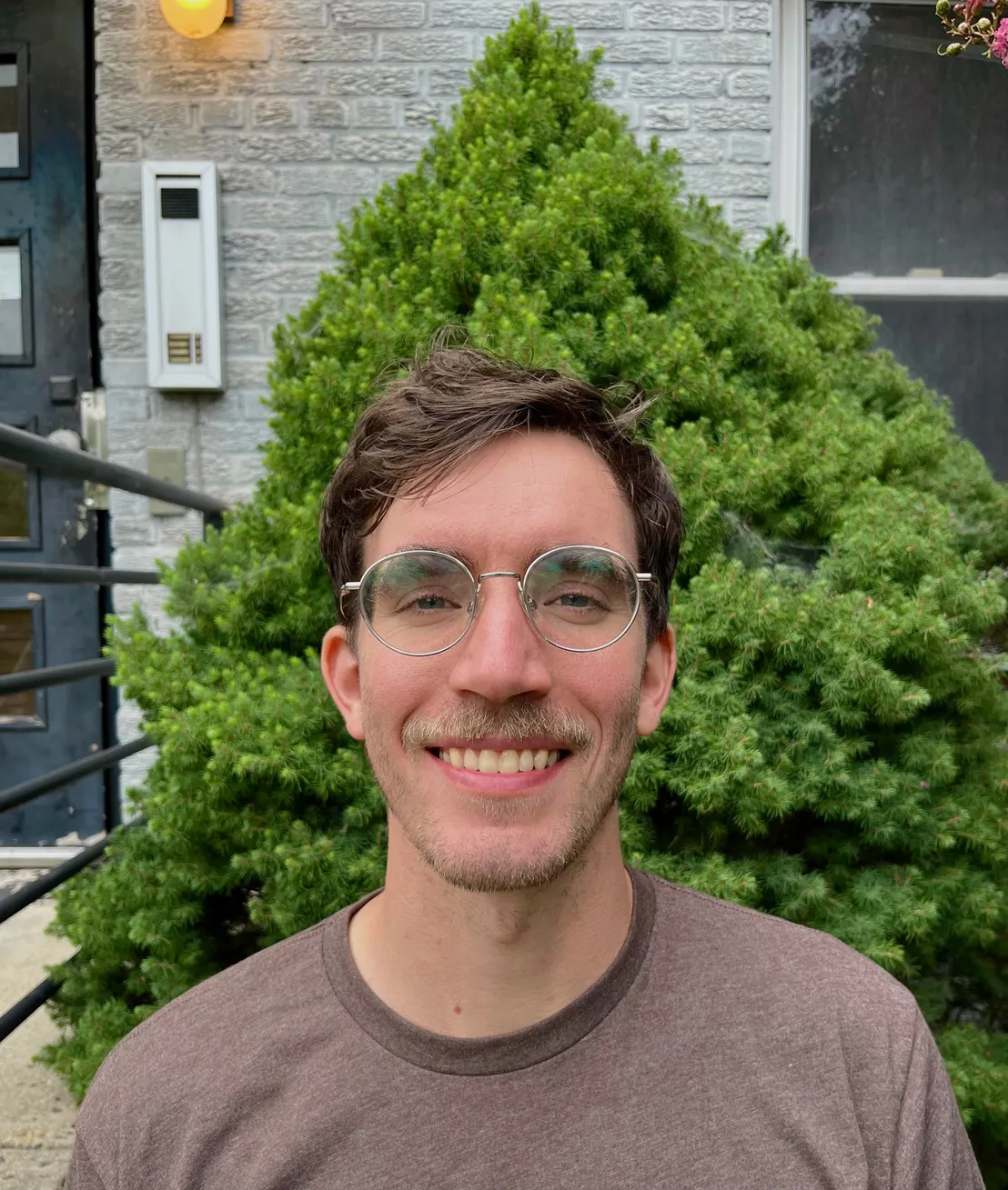 Josh Mahan smiling in front of a leafy green shrub